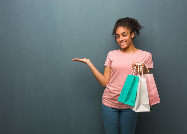 Joven mujer negra sosteniendo algo con la mano. Ella está sosteniendo una bolsa de compras.