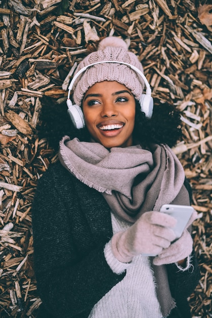 Joven mujer negra en el teléfono móvil acostado sobre paces de madera cerca del palacio real de Madrid durante el invierno