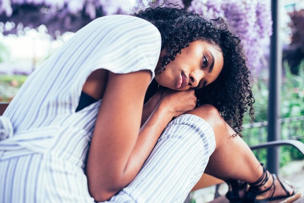 Joven mujer negra triste sentada rodeada de flores