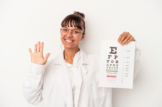 Joven mujer óptica de raza mixta haciendo una prueba aislada sobre fondo blanco sonriendo alegre mostrando el número cinco con los dedos.