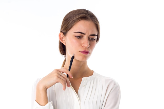 Joven mujer pensativa con blusa blanca sosteniendo un bolígrafo negro en la mano sobre fondo blanco en el estudio