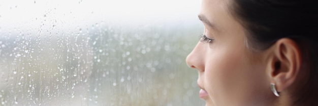 Joven mujer pensativa mirando por la ventana a la lluvia. Concepto de soledad y tristeza