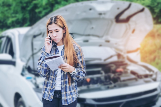 joven mujer pidiendo ayuda con su coche roto por el borde de la carretera