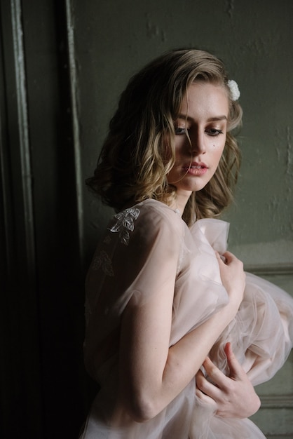 Joven mujer posando en un vestido largo ligero tierno rosa en interiores