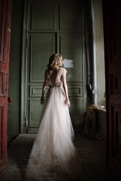 Joven mujer posando en un vestido largo rosa de espaldas en el interior