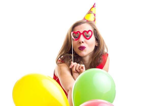 Joven mujer positiva celebrando el sombrero con muchos globos de colores y una tarjeta de gafas