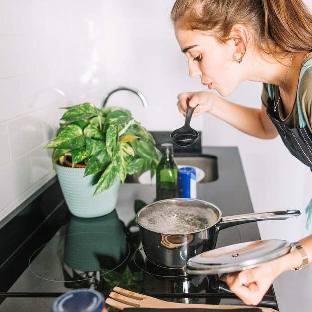 Joven mujer probando la sopa en la cocina