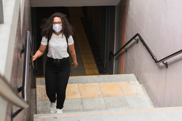 Foto joven mujer que llevaba una máscara médica mientras subía las escaleras