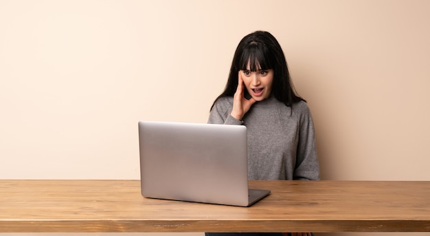 Joven mujer que trabaja con su computadora portátil con sorpresa y expresión facial conmocionada