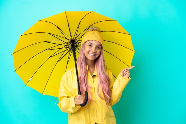 Joven mujer de raza mixta con abrigo impermeable y paraguas apuntando con el dedo hacia el lado