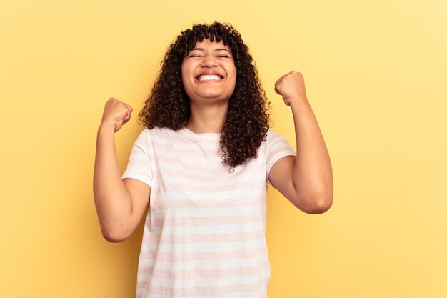 Joven mujer de raza mixta aislada de fondo amarillo celebrando una victoria, pasión y entusiasmo, expresión feliz