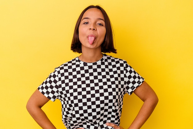 Joven mujer de raza mixta aislada de fondo amarillo divertida y amigable sacando la lengua.