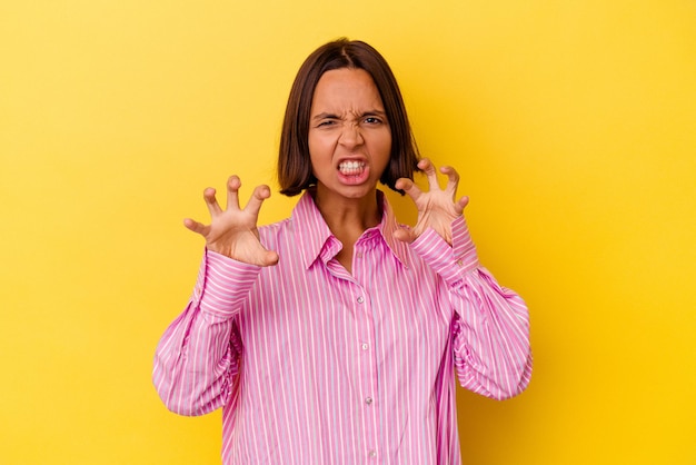 Joven mujer de raza mixta aislada de fondo amarillo mostrando garras imitando a un gato, gesto agresivo.