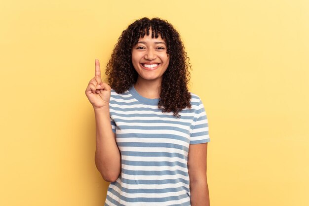 Joven mujer de raza mixta aislada de fondo amarillo que muestra el número uno con el dedo