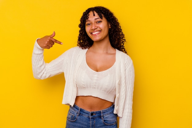 Foto joven mujer de raza mixta aislada sobre fondo amarillo persona apuntando con la mano a un espacio de copia de camisa, orgulloso y seguro