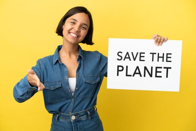 Joven mujer de raza mixta aislada sobre fondo amarillo sosteniendo un cartel con el texto Save the Planet haciendo un trato