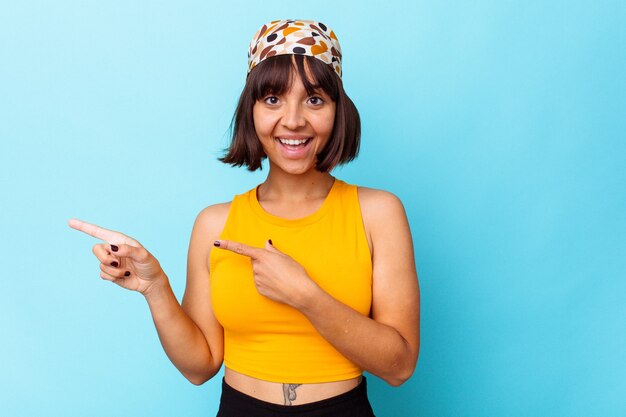 Joven mujer de raza mixta aislada sobre fondo azul sorprendido apuntando con los dedos índices a un espacio de copia.