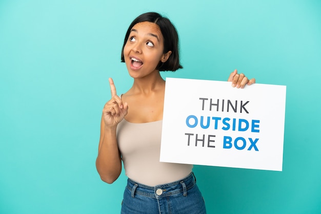 Joven mujer de raza mixta aislada sobre fondo azul sosteniendo una pancarta con texto pensar fuera de la caja y pensar