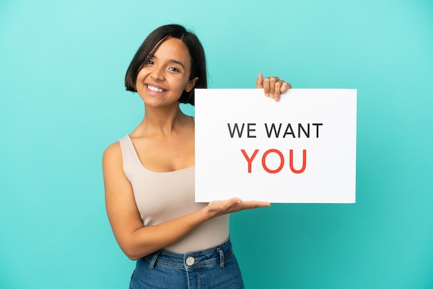 Joven mujer de raza mixta aislada sobre fondo azul sosteniendo We Want You Board con expresión feliz