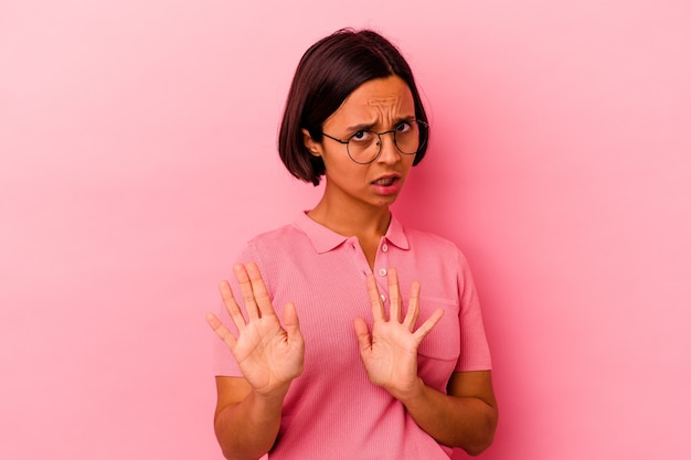 Joven mujer de raza mixta aislada sobre fondo rosa conmocionada debido a un peligro inminente