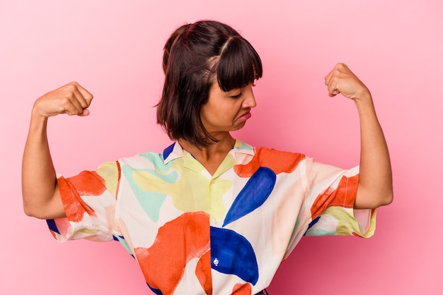 Joven mujer de raza mixta aislada sobre fondo rosa mostrando gesto de fuerza con los brazos, símbolo del poder femenino