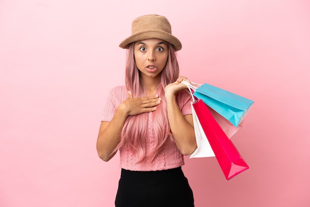Joven mujer de raza mixta con bolsa de compras aislada sobre fondo rosa sorprendida y conmocionada mientras mira a la derecha