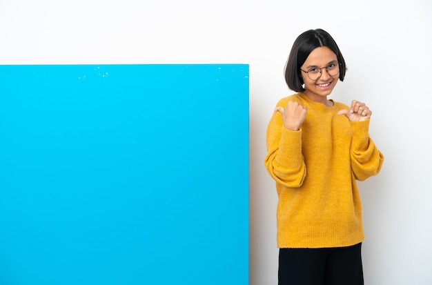 Joven mujer de raza mixta con un gran cartel azul aislado sobre fondo blanco apuntando hacia el lado para presentar un producto