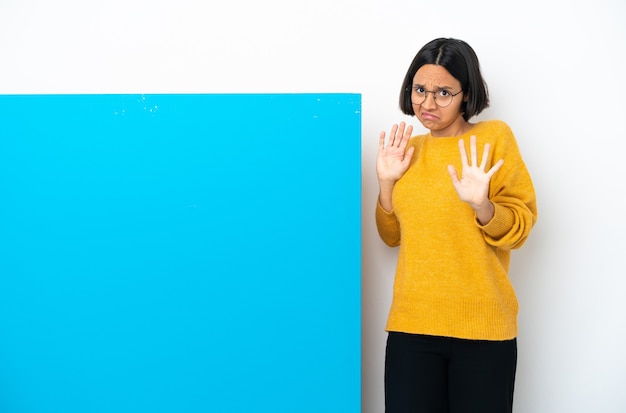 Joven mujer de raza mixta con un gran cartel azul aislado sobre fondo blanco nervioso estirando las manos hacia el frente