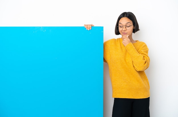 Joven mujer de raza mixta con un gran cartel azul aislado sobre fondo blanco pensando en una idea mientras mira hacia arriba