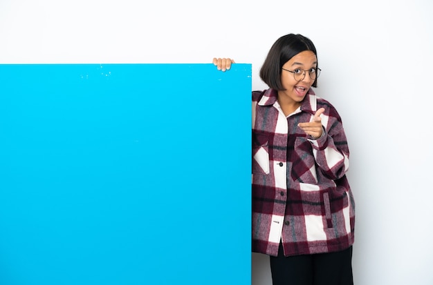 Joven mujer de raza mixta con un gran cartel azul aislado sobre fondo blanco sorprendido y apuntando hacia el frente
