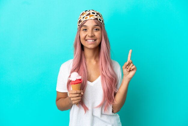 Joven mujer de raza mixta con un helado de cucurucho aislado sobre fondo azul apuntando hacia una gran idea