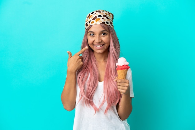 Joven mujer de raza mixta con un helado de cucurucho aislado sobre fondo azul dando un pulgar hacia arriba gesto