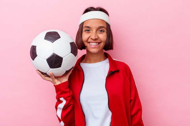 Joven mujer de raza mixta jugando al fútbol aislado en la pared rosa