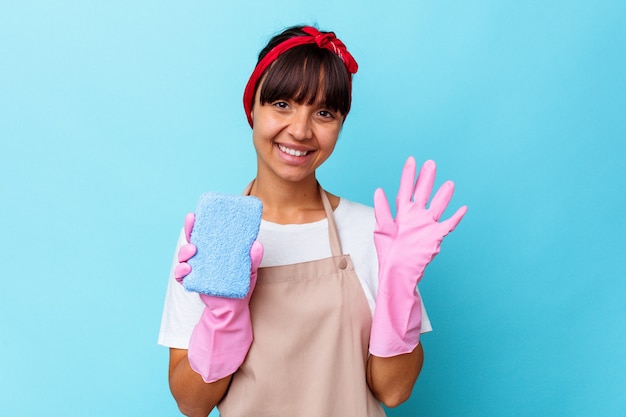 Joven mujer de raza mixta limpieza de casa aislada sobre fondo azul sonriendo alegre mostrando el número cinco con los dedos.