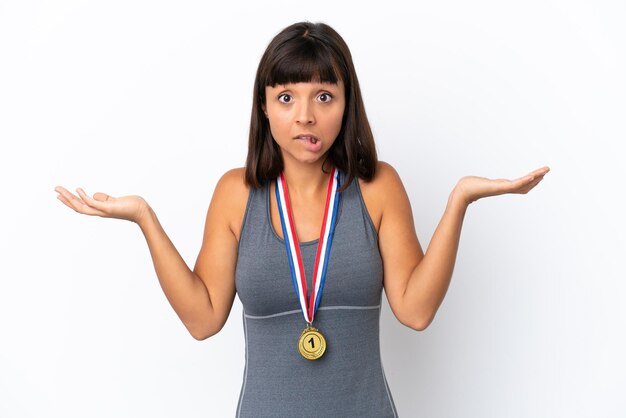 Joven mujer de raza mixta con medallas aisladas de fondo blanco que tiene dudas mientras levanta las manos