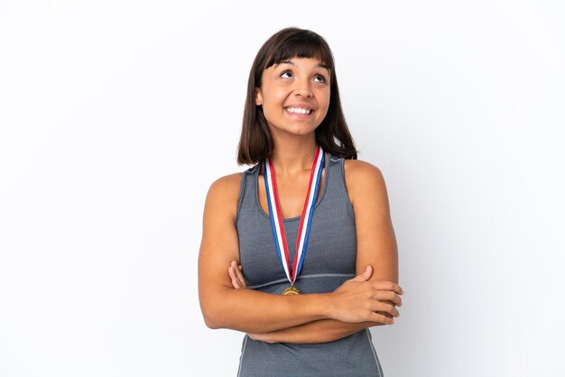 Joven mujer de raza mixta con medallas aislado sobre fondo blanco mirando hacia arriba mientras sonríe