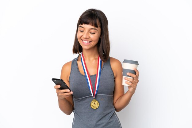 Joven mujer de raza mixta con medallas aislado sobre fondo blanco sosteniendo un café para llevar y un móvil