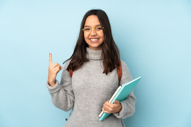 Joven mujer de raza mixta que va a la escuela aislada sobre fondo azul apuntando hacia una gran idea