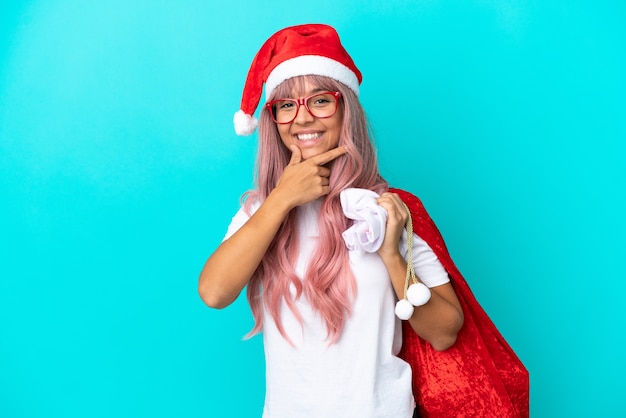 Joven mujer de raza mixta repartiendo regalos en Navidad aislado sobre fondo azul feliz y sonriente