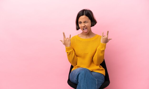 Joven mujer de raza mixta sentado en una silla aislada haciendo gesto de bocina