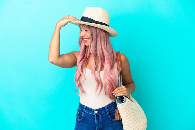 Foto joven mujer de raza mixta sosteniendo una bolsa de playa con pamela aislado sobre fondo azul se ha dado cuenta de algo y tiene la intención de la solución