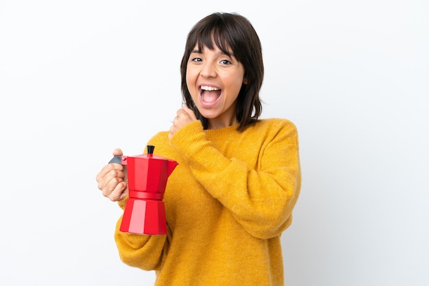 Joven mujer de raza mixta sosteniendo una cafetera aislada de fondo blanco celebrando una victoria