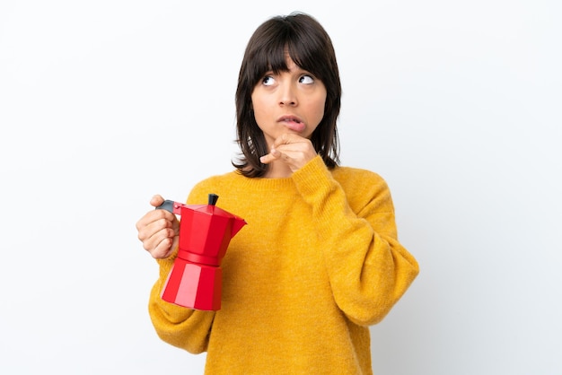 Joven mujer de raza mixta sosteniendo una cafetera aislada de fondo blanco con dudas y pensando