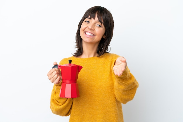 Joven mujer de raza mixta sosteniendo una cafetera aislada de fondo blanco estrechando la mano para cerrar un buen trato