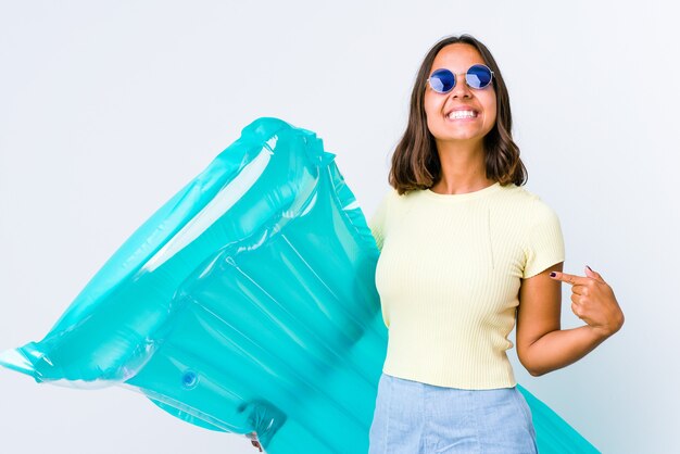 Joven mujer de raza mixta sosteniendo un colchón de aire apunta hacia abajo con los dedos, sentimiento positivo.