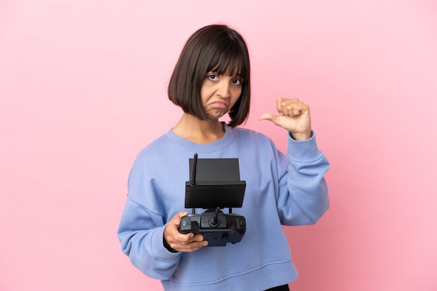 Joven mujer de raza mixta sosteniendo un control remoto de drone aislado sobre fondo rosa orgulloso y satisfecho de sí mismo