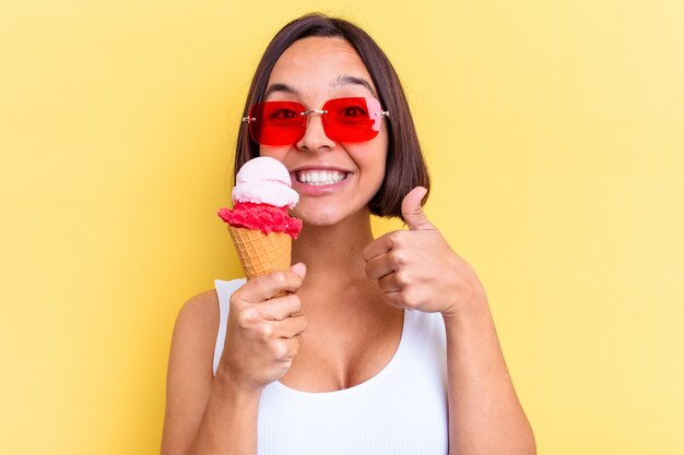 Joven mujer de raza mixta sosteniendo un helado aislado sobre fondo amarillo