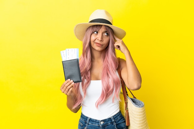 Joven mujer de raza mixta sosteniendo pasaporte y bolsa de playa aislada sobre fondo amarillo con dudas y pensamiento