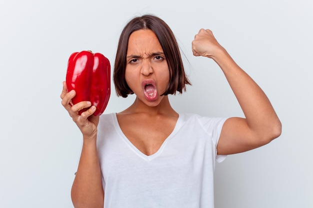 Joven mujer de raza mixta sosteniendo un pimiento aislado en la pared blanca