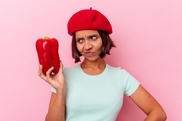 Joven mujer de raza mixta sosteniendo un pimiento aislado en la pared blanca